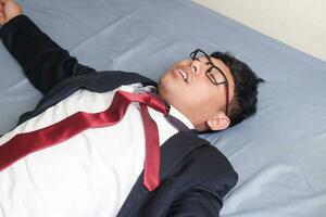 Portrait of young Asian business man in casual suit utterly defeated in bed with very exhausted expressions. Isolated image on blue background photo