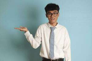 Indonesian senior high school student wearing white shirt uniform with gray tie showing product, pointing at something and smiling. Isolated image on blue background photo