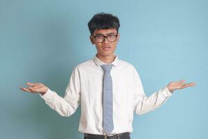 Confused senior high school student wearing white shirt uniform with gray tie spreading his hands sideways and holding two things, demonstrate products. Isolated image on white background photo