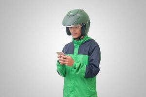 Portrait of Asian online taxi driver wearing green jacket and helmet holding a mobile phone and smiling. Advertising concept. Isolated image on white background photo