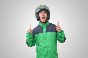 Portrait of Asian online taxi driver wearing green jacket and helmet pointing at empty space with finger. Isolated image on white background photo