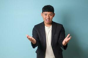 Portrait of young Asian business man in casual suit presenting happily with full confidence. Isolated image on blue background photo