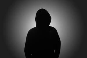 Mysterious man wearing black hoodie standing against dark background. Hacker, crime, and cyber security concept. photo