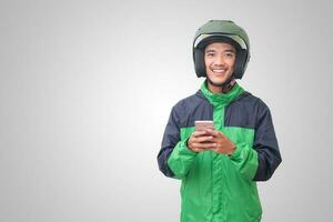 Portrait of Asian online taxi driver wearing green jacket and helmet holding a mobile phone and smiling. Advertising concept. Isolated image on white background photo