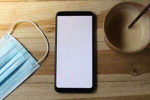 Top view of blank screen mobile phone and medical mask on wooden table photo