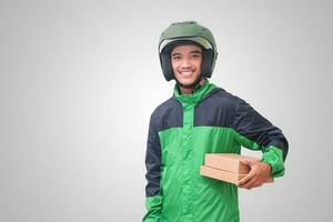 Portrait of Asian online courier driver wearing green jacket and helmet delivering package and box for customer. Isolated image on white background photo