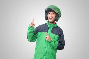 Portrait of Asian online taxi driver wearing green jacket and helmet pointing at empty space with finger. Isolated image on white background photo