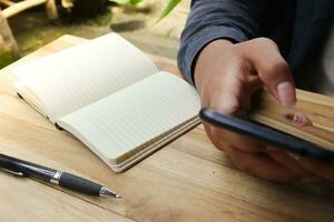 Close up of male hand using mobile phone with empty notebook and a cup of coffee while sitting at cafe photo