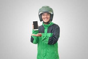 Portrait of Asian online taxi driver wearing green jacket and helmet showing and presenting blank screen mobile phone. Isolated image on white background photo