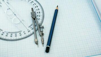 On blue graph paper are compasses, protractor, ruler, and a pencil photo