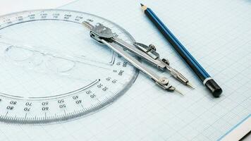 On blue graph paper are compasses, protractor, ruler, and a pencil photo