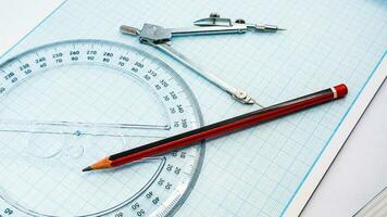 On blue graph paper are compasses, protractor, ruler, and a pencil photo