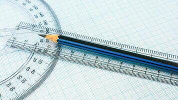 On blue graph paper are compasses, protractor, ruler, and a pencil photo