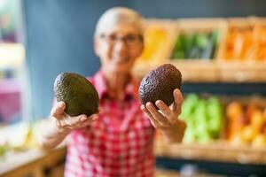 Worker in fruits and vegetables shop is holding avocado. Close up of avocado. photo