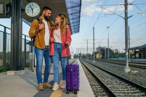 Happy couple is standing at railway station and waiting for arrival of their train. photo