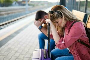 cansado Pareja sentado a ferrocarril estación y esperando para llegada de su tren. foto