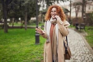 Caucasian ginger woman with freckles and curly hair. is talking on phone in park. photo