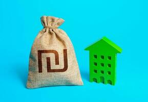 Israeli shekel money bag and green resident building. Investment in green technologies. Reduced emissions and improved energy efficiency. Reducing impact on environment. Sustainable housing. photo