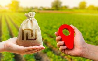 Hands with location pin and israeli shekel money bag. Land market. Transport and construction industry. Buying and selling land. Estimation cost of plots. Agriculture agribusiness. photo