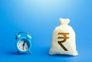 Time and indian rupee money bag. Loans, mortgages. Deposits, savings. Retirement funds. ROI. Bonds, dividends. Bank, finance. Investments. Hourly pay. Time of payment in the contract. Taxation photo