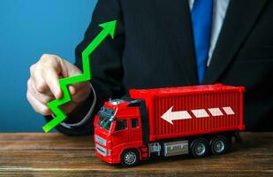 Businessman holds a green arrow up and a truck. Production growth. Import, export. End of containers shortage crisis. Transportation inflation, high shipping rates. Priced rise. Increase in traffic. photo