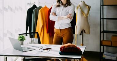 Fashion designer l young asian woman working using laptop, tablet and smiling while standing in workshop Responding on business photo