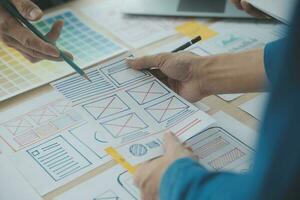 Close up ux developer and ui designer brainstorming about mobile app interface wireframe design on table with customer breif and color code at modern office.Creative digital development agency photo