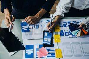 Close up ux developer and ui designer brainstorming about mobile app interface wireframe design on table with customer breif and color code at modern office.Creative digital development agency photo