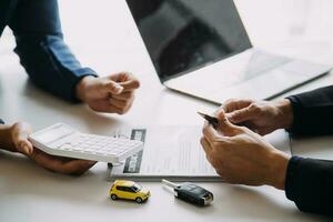 A car rental company employee is handing out the car keys to the renter after discussing the rental details and conditions together with the renter signing a car rental agreement. Concept car rental. photo