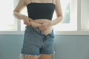 Close up of a belly with scar from c-section and abdominal fat. Women's health. A woman dressed up in sportswear demonstrating her imperfect body after a childbirth with nursery on the background. photo