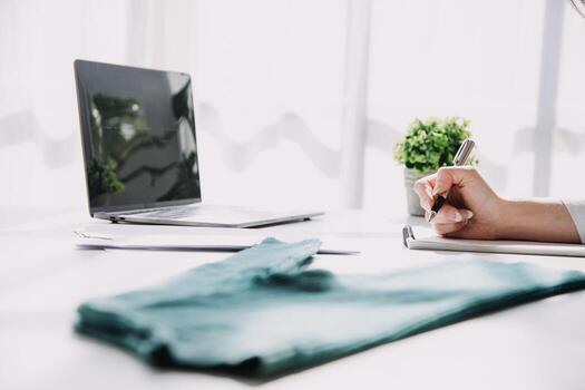 Moda diseñador l joven asiático mujer trabajando utilizando computadora portátil, tableta y sonriente mientras en pie en taller respondiendo en negocio foto
