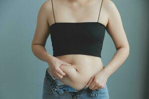 Close up of a belly with scar from c-section and abdominal fat. Women's health. A woman dressed up in sportswear demonstrating her imperfect body after a childbirth with nursery on the background. photo