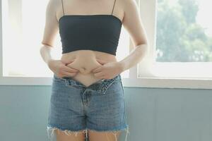 Close up of a belly with scar from c-section and abdominal fat. Women's health. A woman dressed up in sportswear demonstrating her imperfect body after a childbirth with nursery on the background. photo