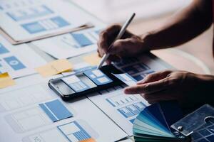 Close up ux developer and ui designer brainstorming about mobile app interface wireframe design on table with customer breif and color code at modern office.Creative digital development agency photo