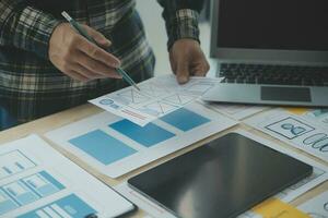 Close up ux developer and ui designer brainstorming about mobile app interface wireframe design on table with customer breif and color code at modern office.Creative digital development agency photo