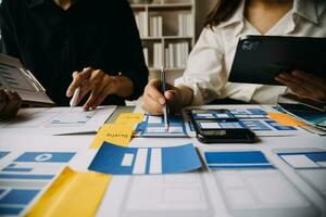 Close up ux developer and ui designer brainstorming about mobile app interface wireframe design on table with customer breif and color code at modern office.Creative digital development agency photo