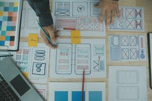 Close up ux developer and ui designer brainstorming about mobile app interface wireframe design on table with customer breif and color code at modern office.Creative digital development agency photo