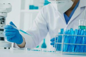 medical or scientific researcher researching and experimenting Multi-colored solution, vial and microscope In the laboratory or in the laboratory by wearing blue gloves and white clothing completely. photo