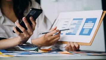 Close up ux developer and ui designer brainstorming about mobile app interface wireframe design on table with customer breif and color code at modern office.Creative digital development agency photo