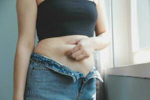 Close up of a belly with scar from c-section and abdominal fat. Women's health. A woman dressed up in sportswear demonstrating her imperfect body after a childbirth with nursery on the background. photo