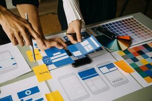 Close up ux developer and ui designer brainstorming about mobile app interface wireframe design on table with customer breif and color code at modern office.Creative digital development agency photo