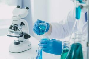 medical or scientific researcher researching and experimenting Multi-colored solution, vial and microscope In the laboratory or in the laboratory by wearing blue gloves and white clothing completely. photo