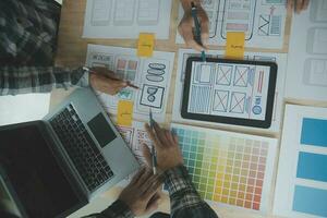 Close up ux developer and ui designer brainstorming about mobile app interface wireframe design on table with customer breif and color code at modern office.Creative digital development agency photo