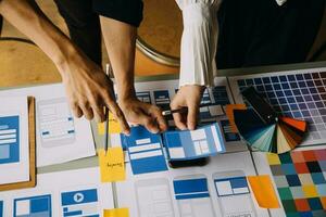 Close up ux developer and ui designer brainstorming about mobile app interface wireframe design on table with customer breif and color code at modern office.Creative digital development agency photo