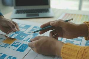 Close up ux developer and ui designer brainstorming about mobile app interface wireframe design on table with customer breif and color code at modern office.Creative digital development agency photo