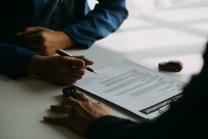 A car rental company employee is handing out the car keys to the renter after discussing the rental details and conditions together with the renter signing a car rental agreement. Concept car rental. photo