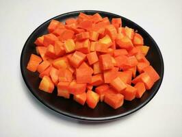 Diced carrots on black plate, white background. photo