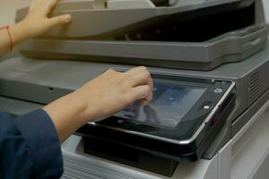 The secretary presses a finger on the keypad on the copier's screen to set up a print job to make multiple copies of a document. soft and selective focus photo