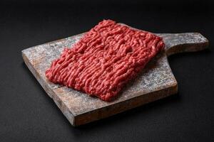 Raw ground beef or pork on a wooden cutting board with spices and salt photo