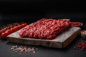 Raw ground beef or pork on a wooden cutting board with spices and salt photo